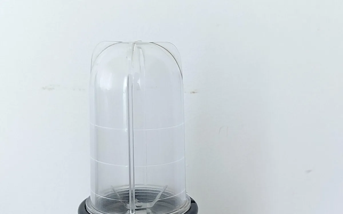 An inverted clear blender cup with visible blades rests on a black base against a pale background