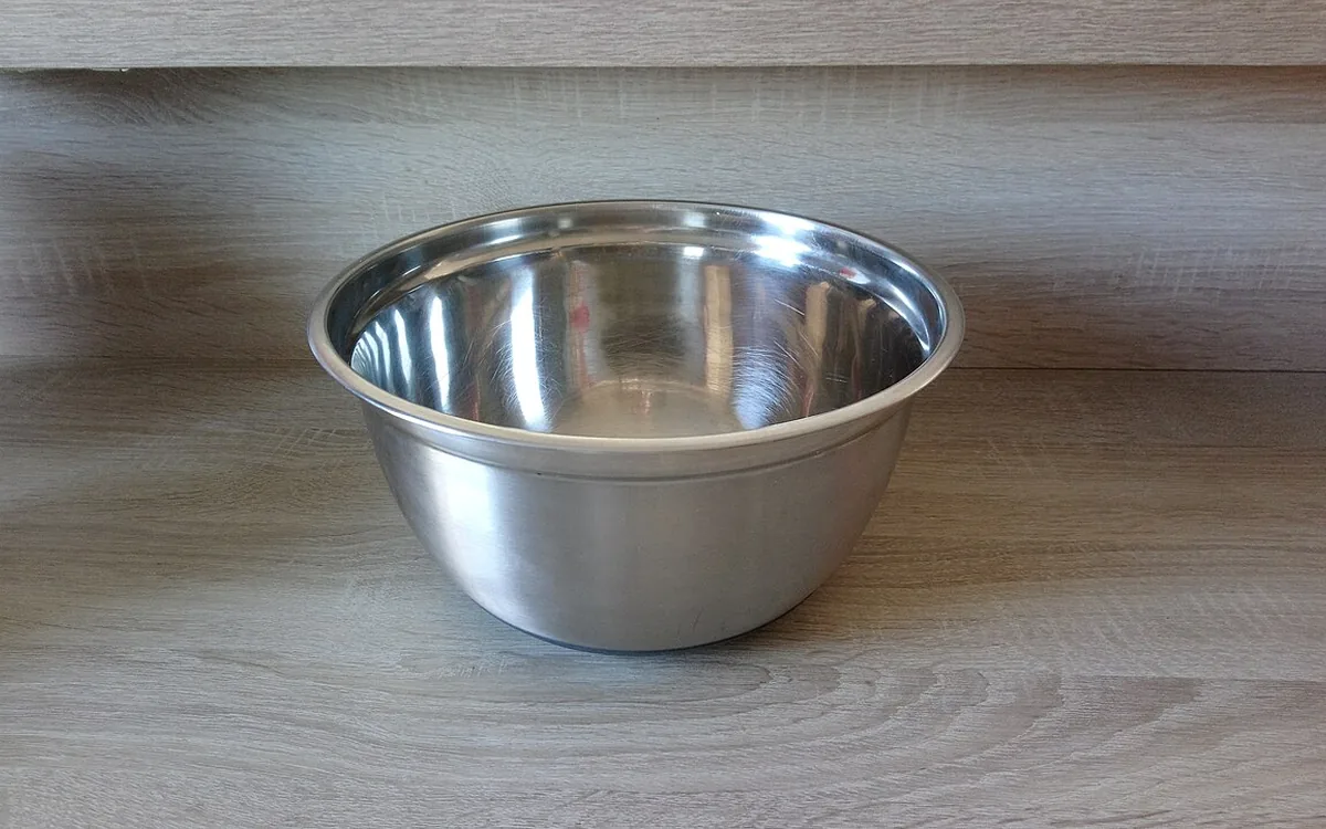 An empty stainless steel mixing bowl on a wood-grain kitchen counter.