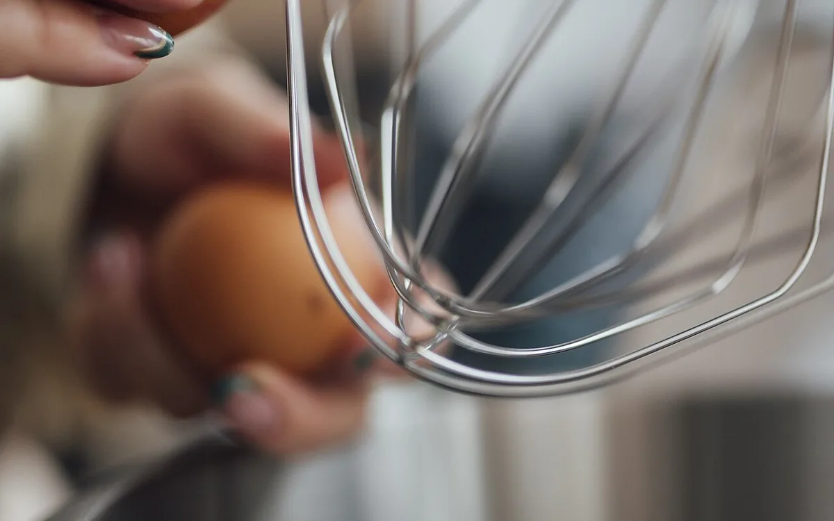 Close-up of a metal wire whisk with a person's fingers visible behind it.