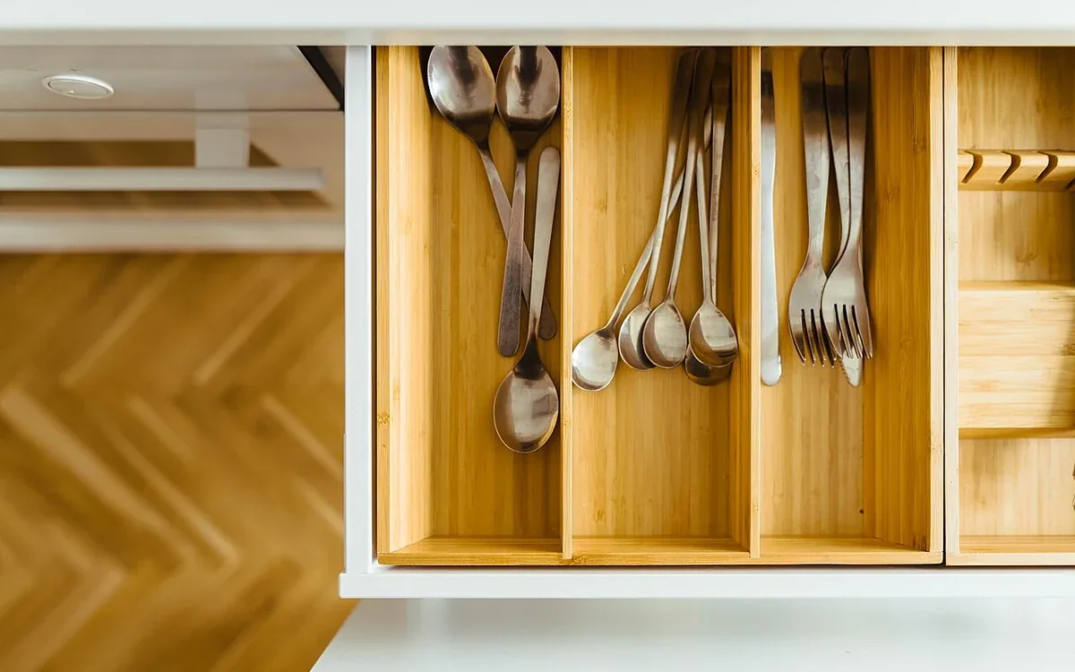 Metal spoons, forks and other utensils rest in separate compartments of an open wooden kitchen drawer