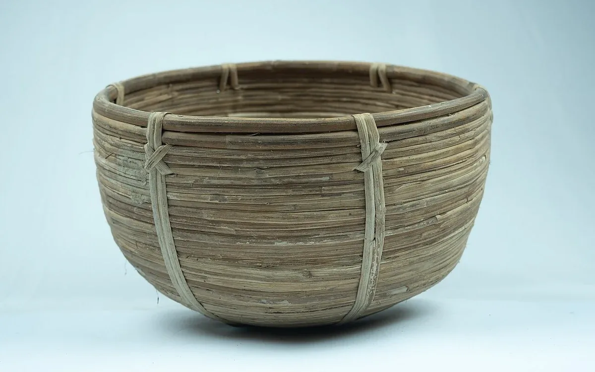 A round woven basket with two handles and a wide open top sits alone against a pale blue background