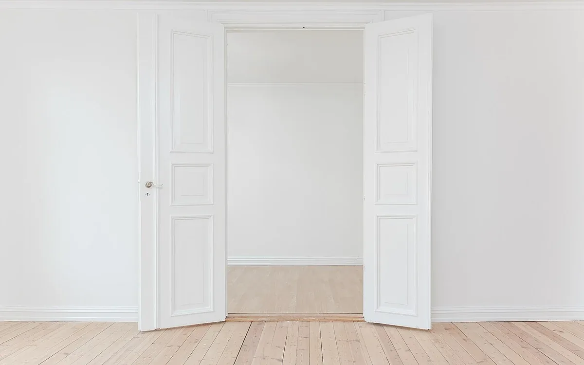 Open white double doors lead into an empty pale-walled room with light wooden flooring