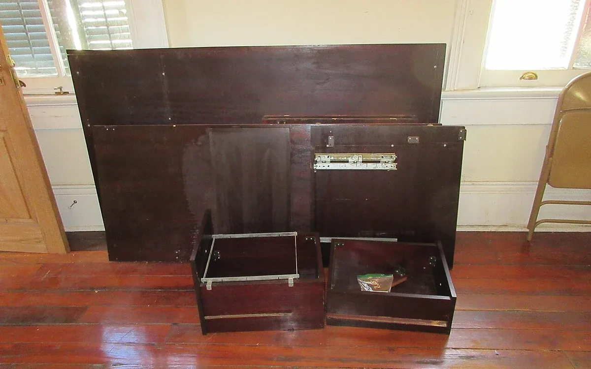 Several dark wooden furniture panels and two small drawer units rest on a wooden floor against a pale wall